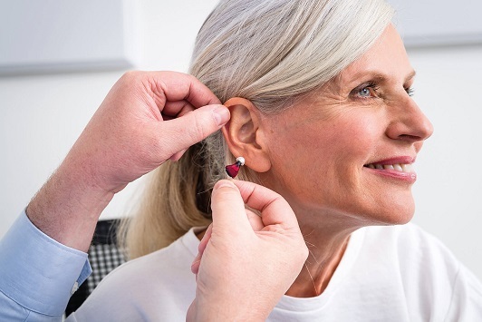 Eine Frau bekommt ein modernes Hörgerät angepasst und lächelt zufrieden im Hörzentrum.